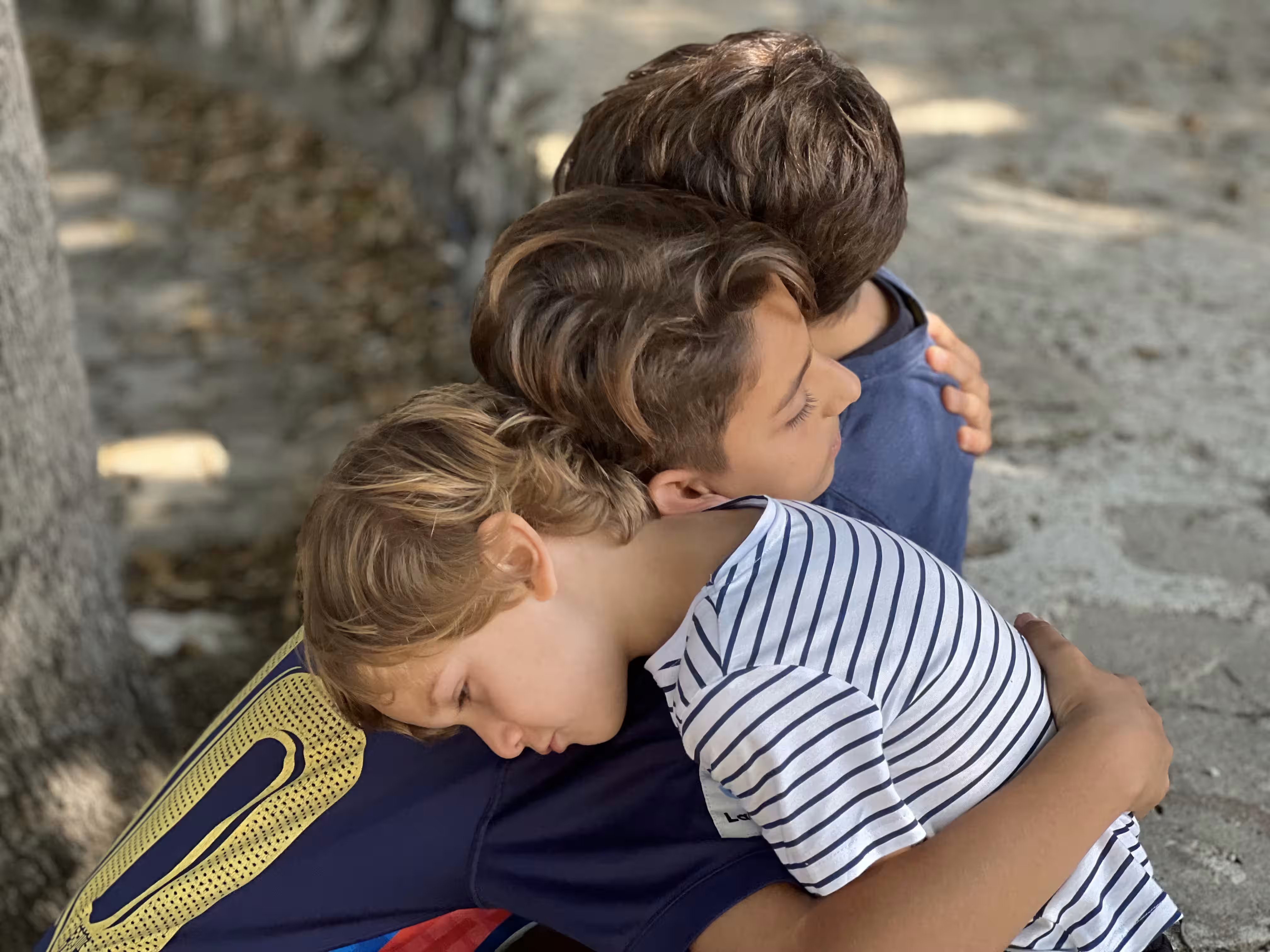 Three young children embracing protectively and sharing a somber moment outdoors.